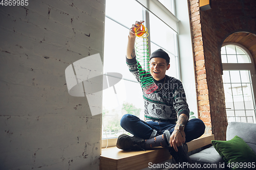 Image of Portrait of millenial boy using retro toys, meeting things from the past and having fun, exploring rainbow spring toy