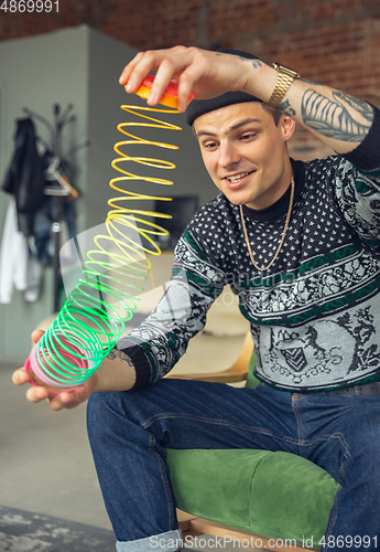 Image of Portrait of millenial boy using retro toys, meeting things from the past and having fun, exploring rainbow spring toy