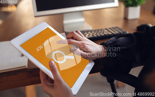 Image of Female hands scrolling tablet while looking for a job during worldwide crisis of coronavirus pandemic. Find a job online. Business, internet and networking concept.