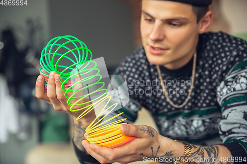 Image of Portrait of millenial boy using retro toys, meeting things from the past and having fun, exploring rainbow spring toy