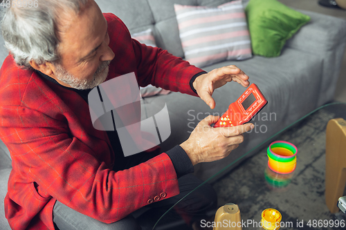 Image of Portrait of senior man with retro toys, meeting things from the past and having fun, exploring the lifestyle of the nineties, playing with rainbow spring toy and tetris