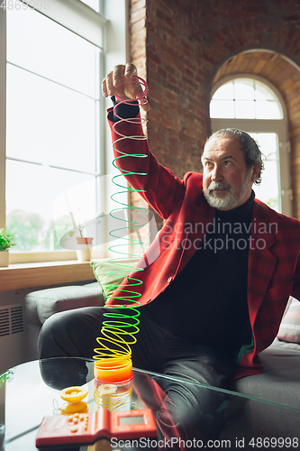 Image of Portrait of senior man with retro toys, meeting things from the past and having fun, exploring the lifestyle of the nineties, playing with rainbow spring toy