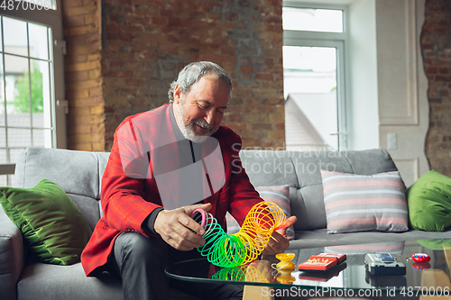 Image of Portrait of senior man with retro toys, meeting things from the past and having fun, exploring the lifestyle of the nineties, playing with rainbow spring toy