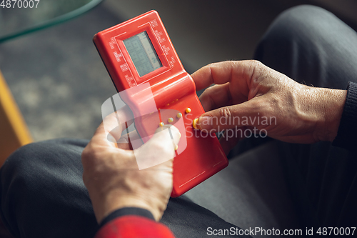 Image of Close up of senior man with retro toys, meeting things from the past and having fun, exploring the lifestyle of the nineties, playing with tetris