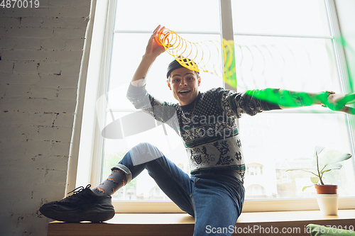 Image of Portrait of millenial boy using retro toys, meeting things from the past and having fun, exploring rainbow spring toy