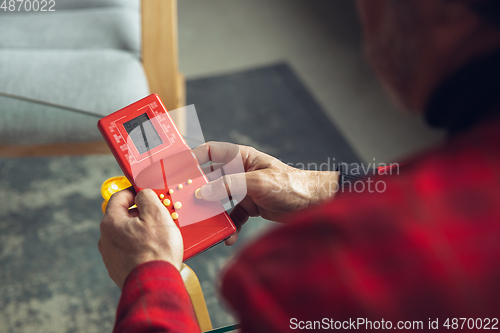 Image of Close up of senior man with retro toys, meeting things from the past and having fun, exploring the lifestyle of the nineties, playing with tetris