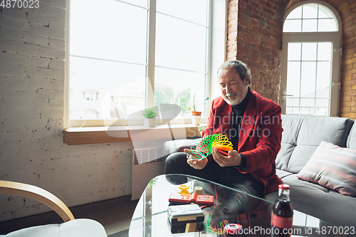 Image of Portrait of senior man with retro toys, meeting things from the past and having fun, exploring the lifestyle of the nineties, playing with rainbow spring toy