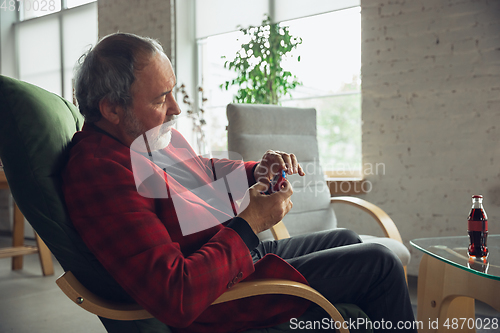 Image of Portrait of senior man with retro toys, meeting things from the past and having fun, exploring the lifestyle of the nineties, playing with tamagotchi