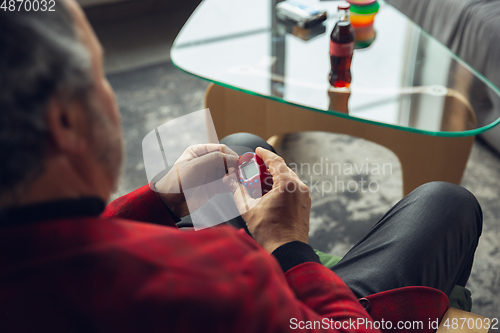 Image of Close up of senior man with retro toys, meeting things from the past and having fun, exploring the lifestyle of the nineties, playing with tamagotchi