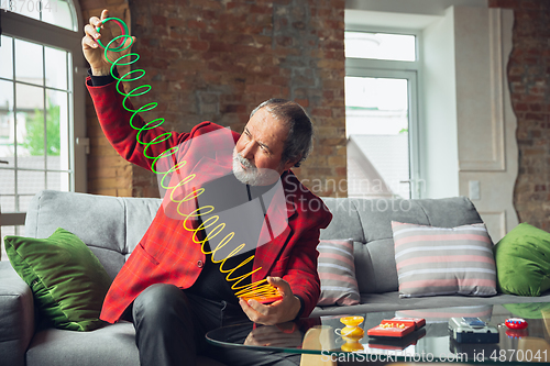 Image of Portrait of senior man with retro toys, meeting things from the past and having fun, exploring the lifestyle of the nineties, playing with rainbow spring toy