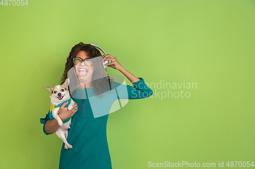 Image of African-american beautiful young woman\'s portrait with little doggy on green studio background, emotional and expressive. Copyspace for ad.