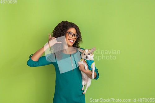 Image of African-american beautiful young woman\'s portrait with little doggy on green studio background, emotional and expressive. Copyspace for ad.