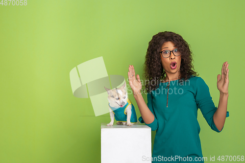 Image of African-american beautiful young woman\'s portrait with little doggy on green studio background, emotional and expressive. Copyspace for ad.