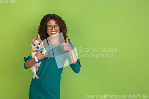 Image of African-american beautiful young woman\'s portrait with little doggy on green studio background, emotional and expressive. Copyspace for ad.