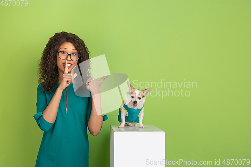 Image of African-american beautiful young woman\'s portrait with little doggy on green studio background, emotional and expressive. Copyspace for ad.
