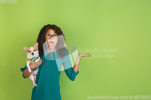 Image of African-american beautiful young woman\'s portrait with little doggy on green studio background, emotional and expressive. Copyspace for ad.