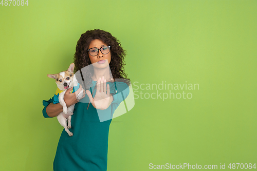 Image of African-american beautiful young woman\'s portrait with little doggy on green studio background, emotional and expressive. Copyspace for ad.