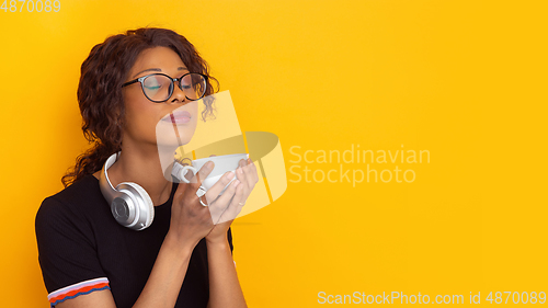 Image of African-american beautiful young woman\'s portrait with wireless headphones on yellow studio background, emotional and expressive. Copyspace for ad.