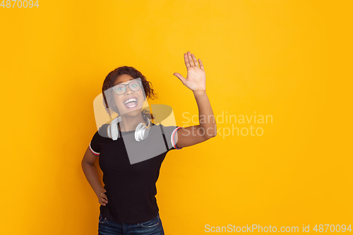 Image of African-american beautiful young woman\'s portrait with wireless headphones on yellow studio background, emotional and expressive. Copyspace for ad.