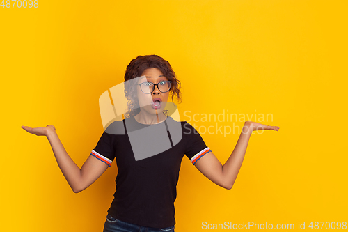 Image of African-american beautiful young woman\'s portrait on yellow studio background, emotional and expressive. Copyspace for ad.