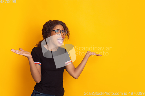 Image of African-american beautiful young woman\'s portrait on yellow studio background, emotional and expressive. Copyspace for ad.