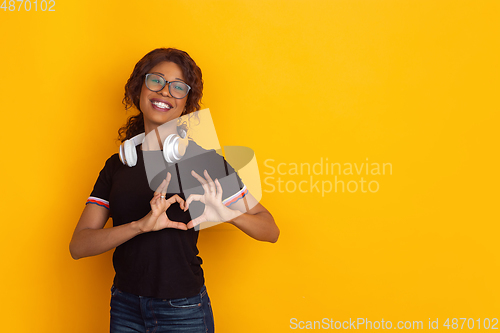 Image of African-american beautiful young woman\'s portrait with wireless headphones on yellow studio background, emotional and expressive. Copyspace for ad.