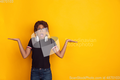 Image of African-american beautiful young woman\'s portrait with wireless headphones on yellow studio background, emotional and expressive. Copyspace for ad.