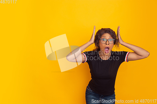 Image of African-american beautiful young woman\'s portrait on yellow studio background, emotional and expressive. Copyspace for ad.