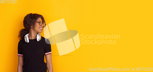 Image of African-american beautiful young woman\'s portrait with wireless headphones on yellow studio background, emotional and expressive. Flyer with copyspace for ad.
