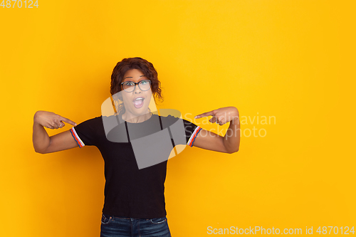 Image of African-american beautiful young woman\'s portrait on yellow studio background, emotional and expressive. Copyspace for ad.