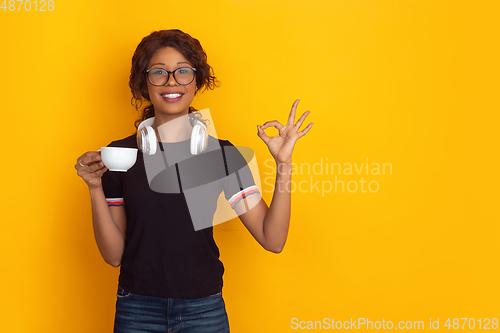 Image of African-american beautiful young woman\'s portrait with wireless headphones on yellow studio background, emotional and expressive. Copyspace for ad.