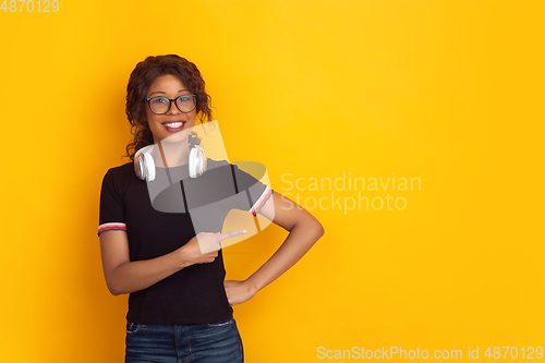 Image of African-american beautiful young woman\'s portrait with wireless headphones on yellow studio background, emotional and expressive. Copyspace for ad.