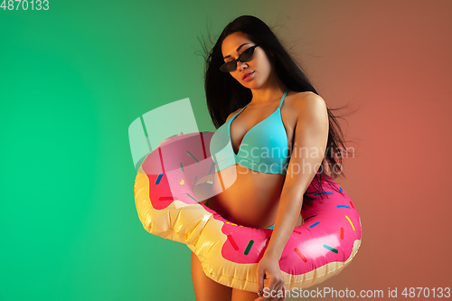 Image of Fashion portrait of young fit and sportive woman in blue luxury swimwear with rubber donut and stylish sunglasses on gradient background. Perfect body ready for summertime.
