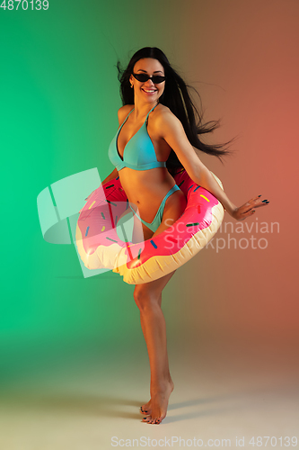 Image of Fashion portrait of young fit and sportive woman in blue luxury swimwear with rubber donut and stylish sunglasses on gradient background. Perfect body ready for summertime.