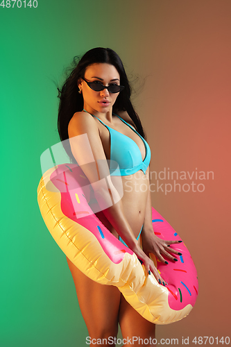 Image of Fashion portrait of young fit and sportive woman in blue luxury swimwear with rubber donut and stylish sunglasses on gradient background. Perfect body ready for summertime.