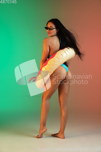 Image of Fashion portrait of young fit and sportive woman in blue luxury swimwear with rubber donut and stylish sunglasses on gradient background. Perfect body ready for summertime.