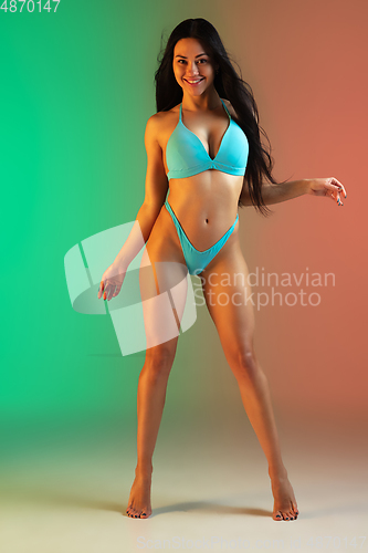 Image of Fashion portrait of young fit and sportive woman in stylish blue luxury swimwear on gradient background. Perfect body ready for summertime.