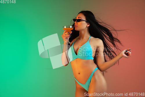 Image of Fashion portrait of young fit and sportive woman in blue luxury swimwear with cocktail and stylish sunglasses on gradient background. Perfect body ready for summertime.