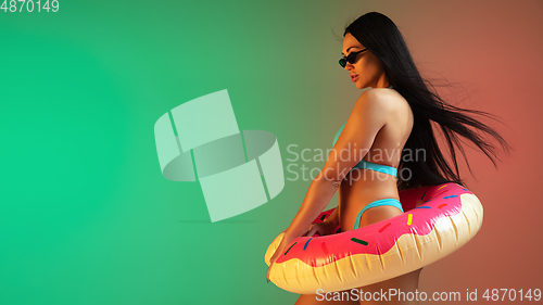 Image of Fashion portrait of young fit and sportive woman in blue luxury swimwear with rubber donut and stylish sunglasses on gradient background. Perfect body ready for summertime. Flyer.