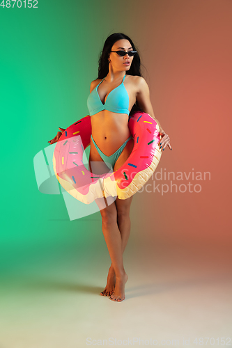 Image of Fashion portrait of young fit and sportive woman in blue luxury swimwear with rubber donut and stylish sunglasses on gradient background. Perfect body ready for summertime.
