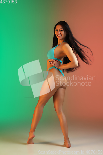Image of Fashion portrait of young fit and sportive woman in stylish blue luxury swimwear on gradient background. Perfect body ready for summertime.