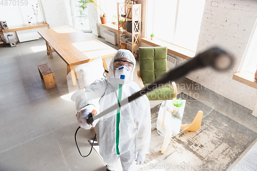 Image of Coronavirus Pandemic. A disinfector in a protective suit and mask sprays disinfectants in the house or office