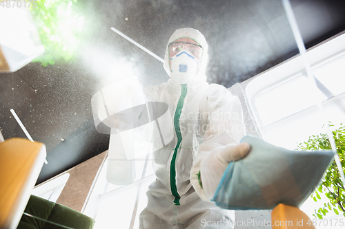 Image of Coronavirus Pandemic. A disinfector in a protective suit and mask sprays disinfectants in the house or office