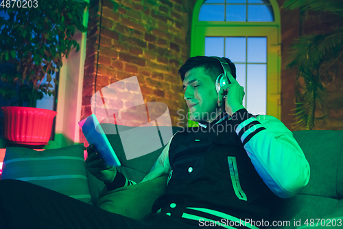 Image of Cinematic portrait of handsome young man using devices, gadgets in neon lighted interior. Youth culture, bright colors