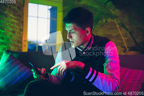 Image of Cinematic portrait of handsome young man using devices, gadgets in neon lighted interior. Youth culture, bright colors