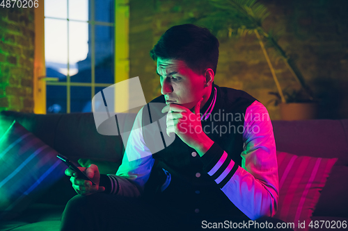 Image of Cinematic portrait of handsome young man using devices, gadgets in neon lighted interior. Youth culture, bright colors