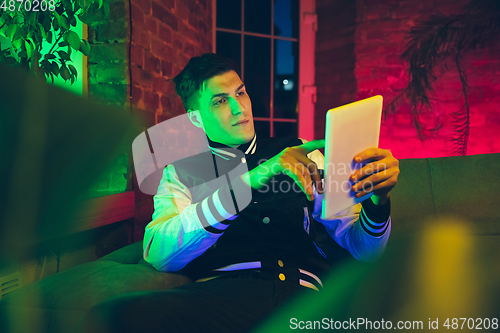 Image of Cinematic portrait of handsome young man using devices, gadgets in neon lighted interior. Youth culture, bright colors