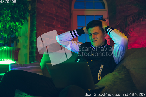 Image of Cinematic portrait of handsome young man using devices, gadgets in neon lighted interior. Youth culture, bright colors