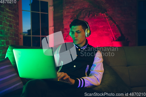 Image of Cinematic portrait of handsome young man using devices, gadgets in neon lighted interior. Youth culture, bright colors