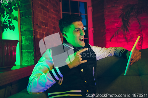 Image of Cinematic portrait of handsome young man using devices, gadgets in neon lighted interior. Youth culture, bright colors